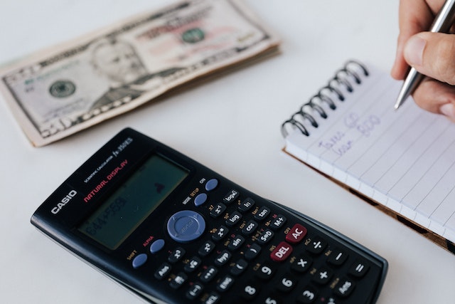 person writing notes with cash and a calculator next to them