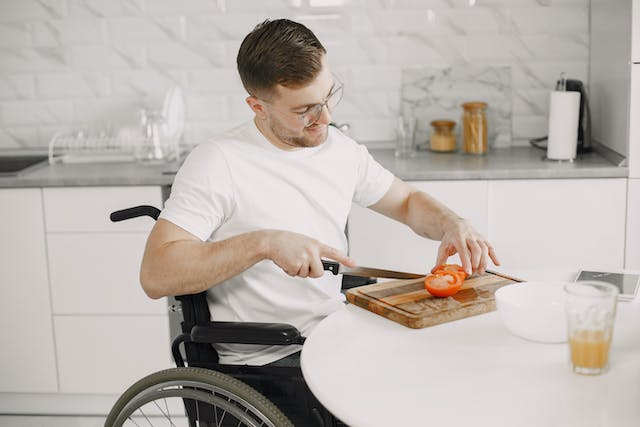 person in a wheelchair cutting a tomato at their kitchen table