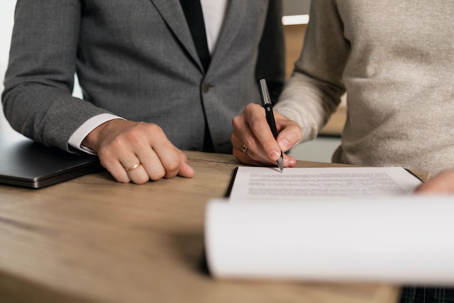 a landlord in a dark suit watching a tenant sign a lease agreement