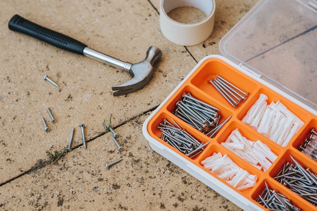 an orange toolbox with nails and screws inside and a hammer next to it