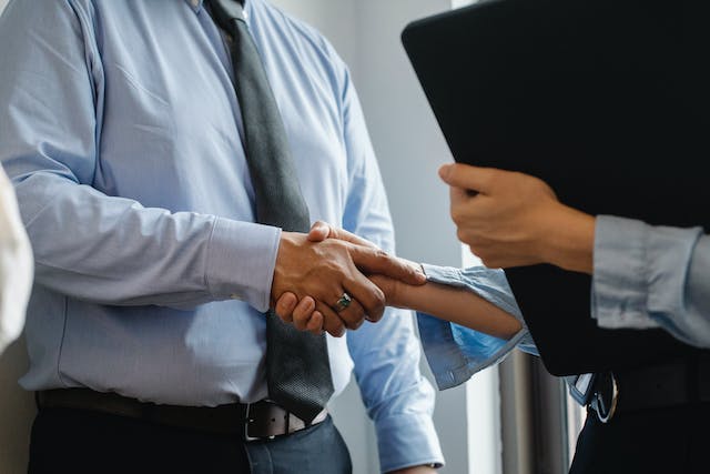 two people shaking hands one holds a folder