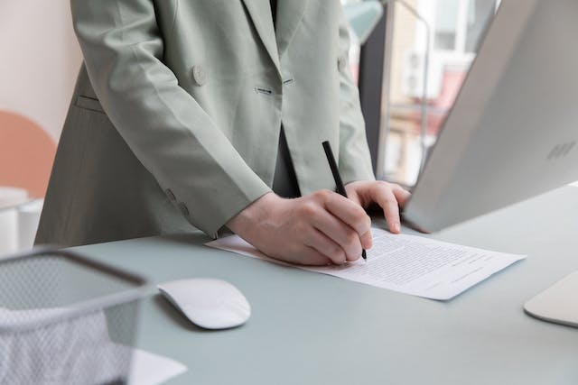 Person in a light green suit signing a contract at their desk